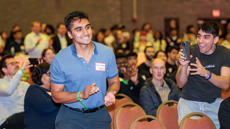 Man clapping and smiling as he emerges from a large crowd at an event