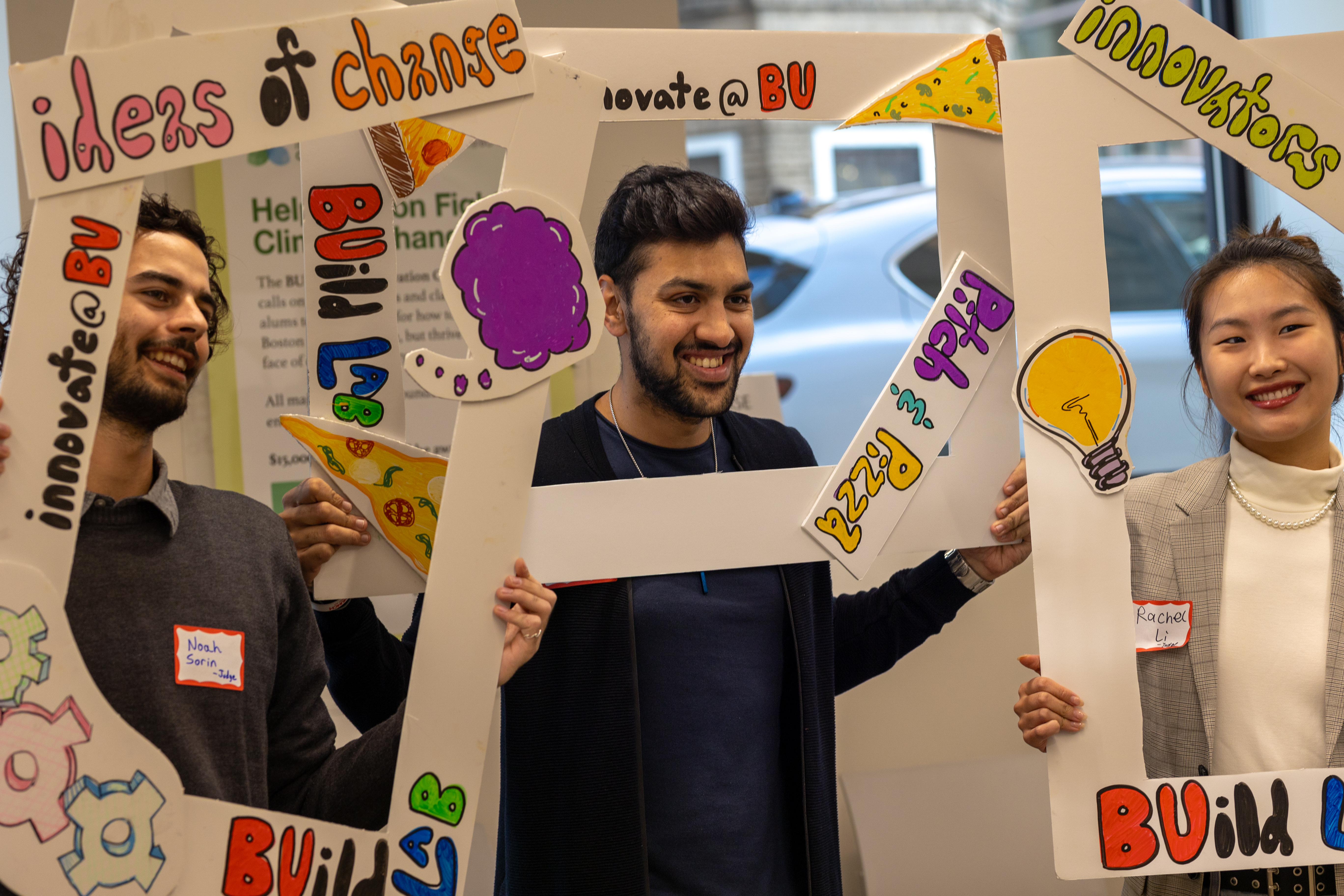 Three students pose with holding decorative frames around their faces at an event