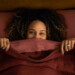 Woman in bed with her eyes peering over the blankets