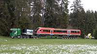 Ein Schwerlasttransport, beladen mit einem Bahnwaggon, fährt auf einem Feldweg 