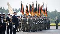 Soldaten stehen mit Musikinstrumenten und Fahnen in Formation.