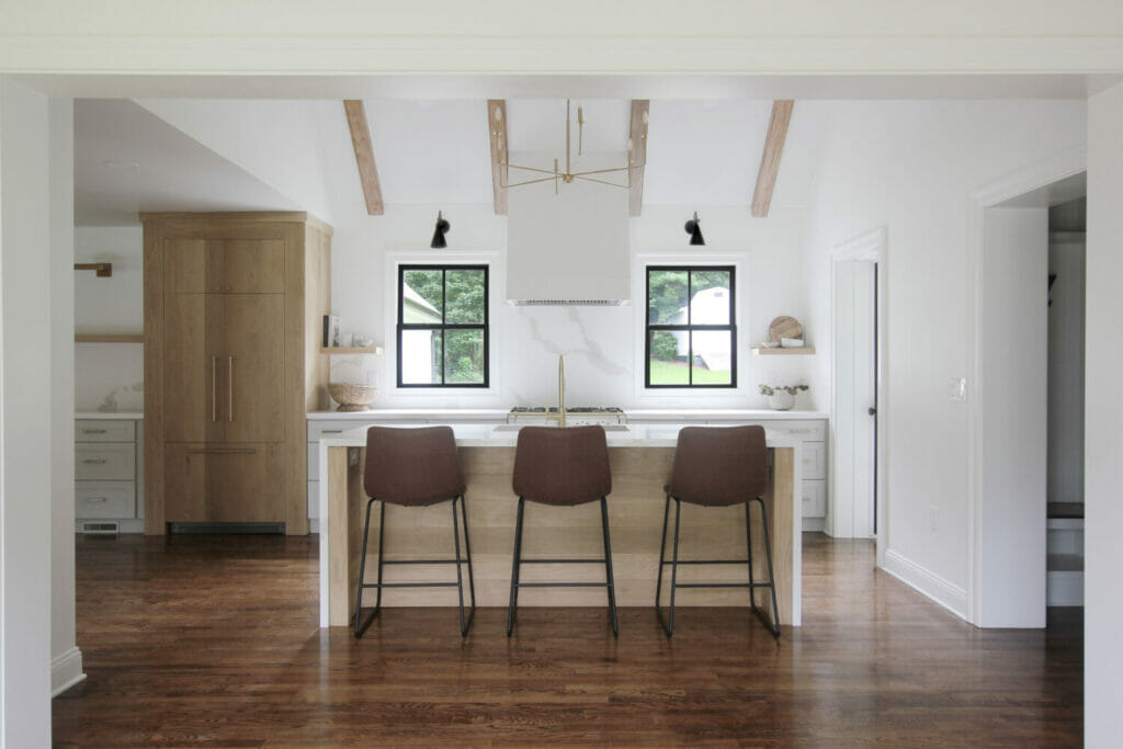 White farmhouse kitchen with Caesarstone's Calacatta Maximus on the kitchen counters and waterfall island, exposed beams, black window frames, and dark floors.