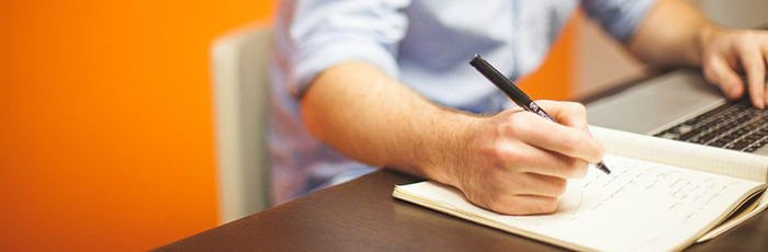 Laptop user writing notes in notebook