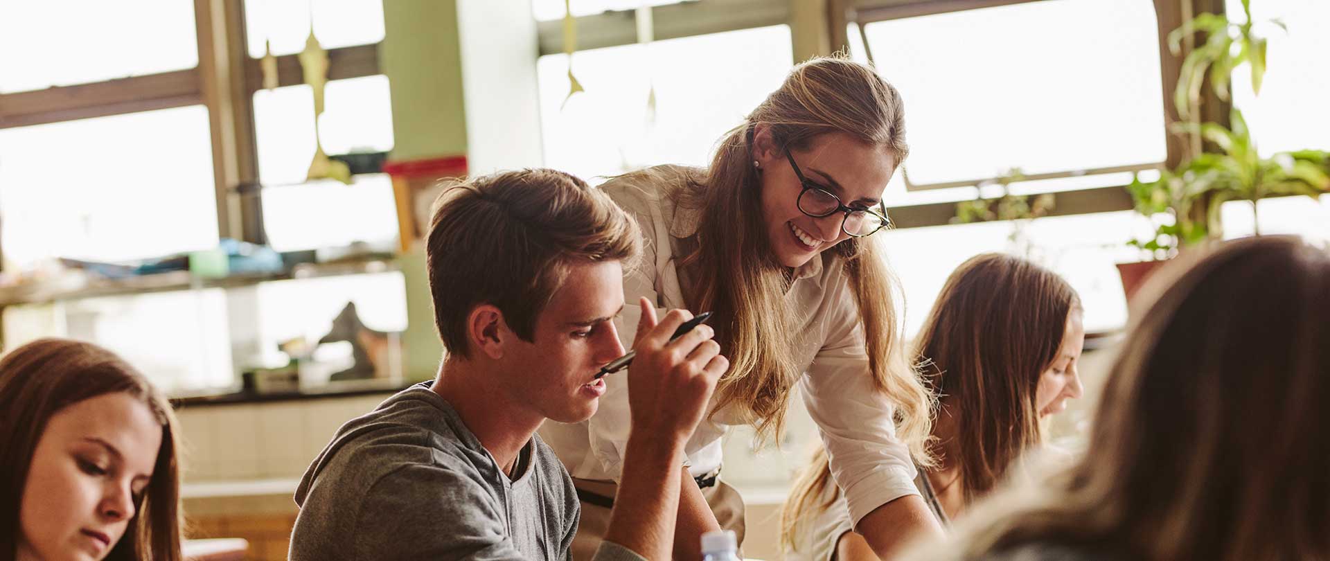 Ein Lehrer steht mit einem Kreidestück in der Hand vor einer Schultafel.