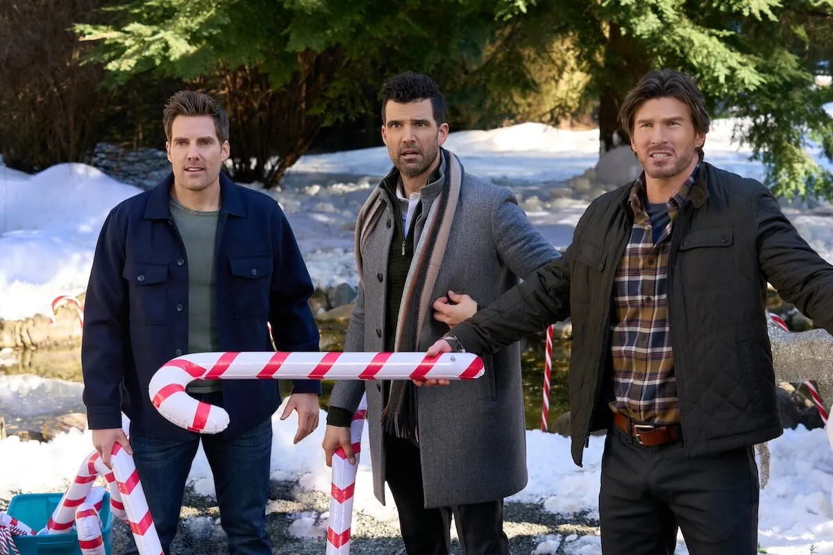 Three men holding a large decorative candy cane in the Hallmark Christmas movie 'Santa Tell Me'