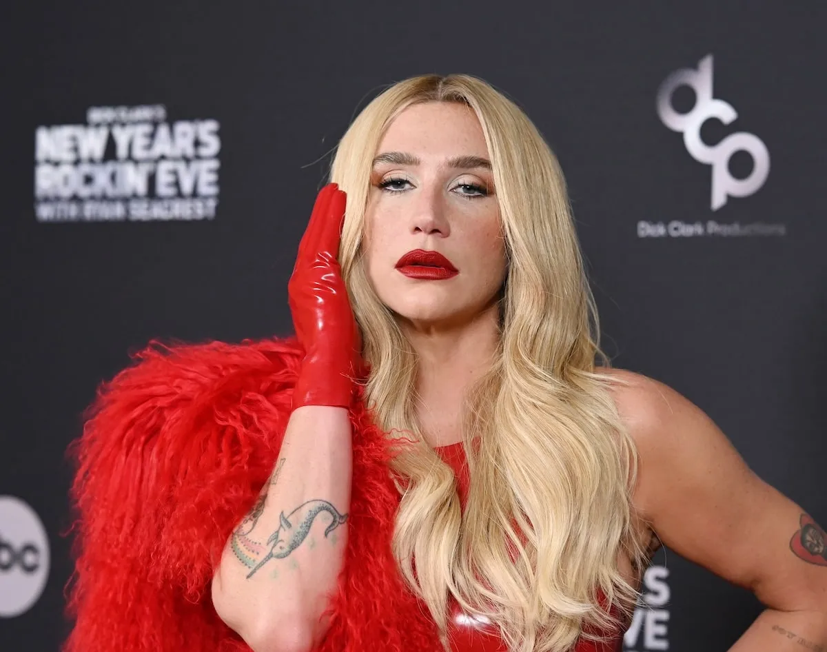 Wearing a red latex bodysuit and large red feather boa, Kesha stands on the red carpet and poses for photos before Dick Clark's New Year's Rockin' Eve with Ryan Seacrest on December 31, 2024