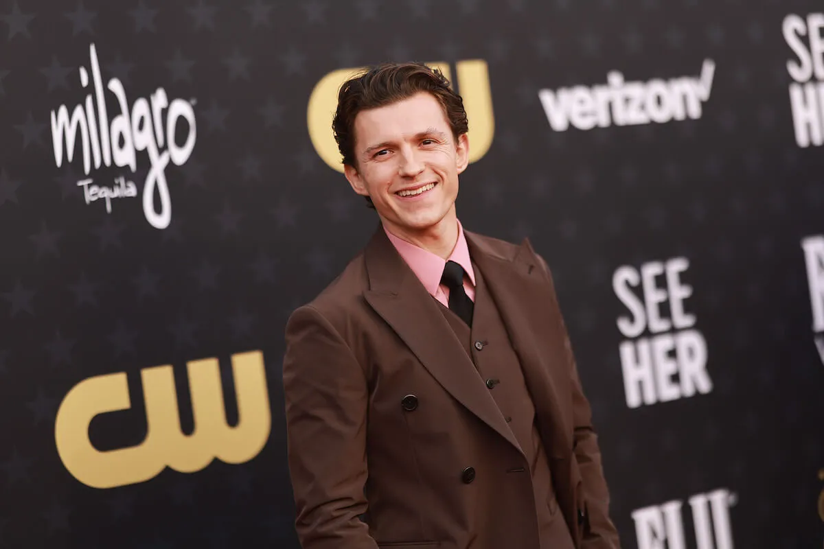 Tom Holland, who quit drinking alcohol in 2022, smiles wearing a brown suit.