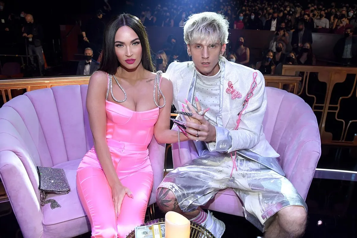 Machine Gun Kelly in a white outfit sitting next to Megan Fox in a pink dress at the 2021 iHeartRadio Music Awards.