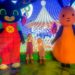 2 small girls stood between and holding hands with 2 large costumed characters from the Kid's TV show, 'Bing'