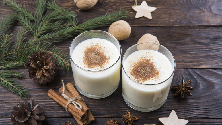 Two glasses of eggnog with holiday decor on a wooden table