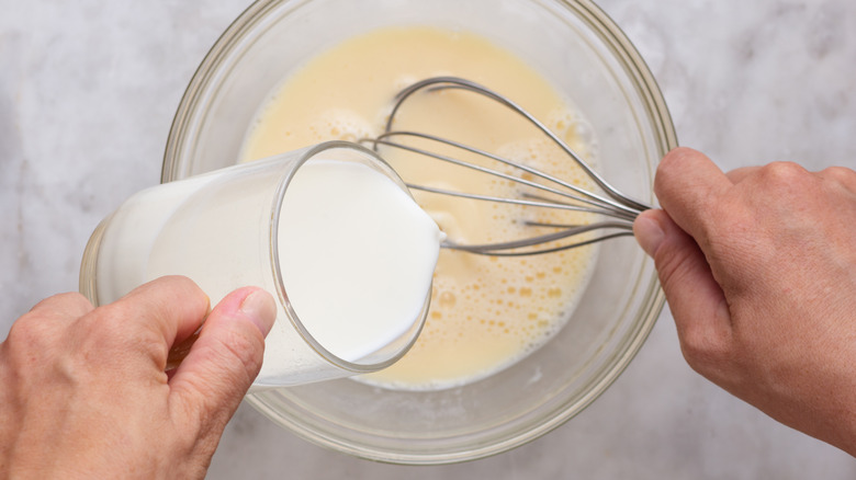 Adding milk to eggs in a glass bowl with whisk