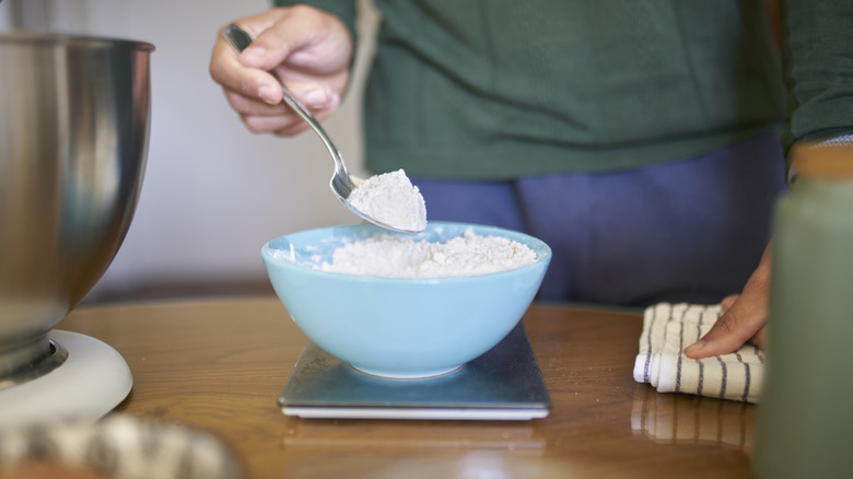 A woman adding flour into a bowl