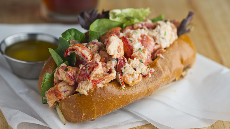 A lobster roll sitting on parchment paper with a small cup of melted butter in the background.