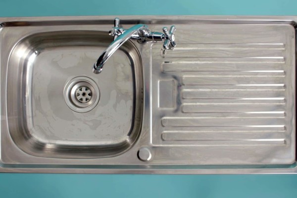 A stainless steel kitchen sink with a faucet and draining board.