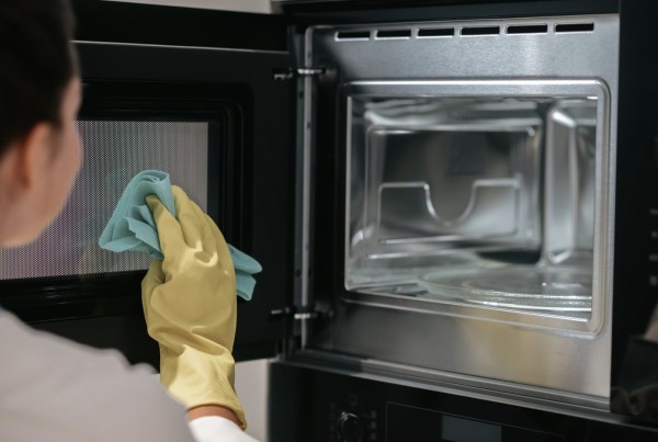 Person cleaning the inside of a microwave oven with a cloth while wearing yellow gloves.