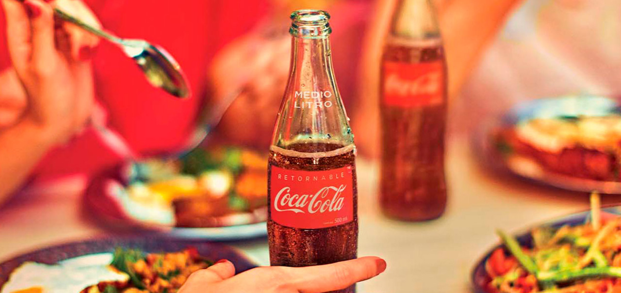 Una mesa servida con comida, refrescos de Coca-Cola y personas conviviendo.