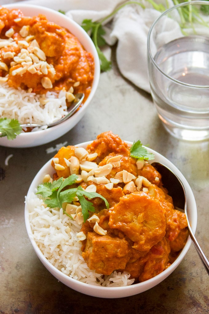 Two Bowls of Smoky Tofu, Peanut Butter & Plantain Curry with Drinking Glass in the Background