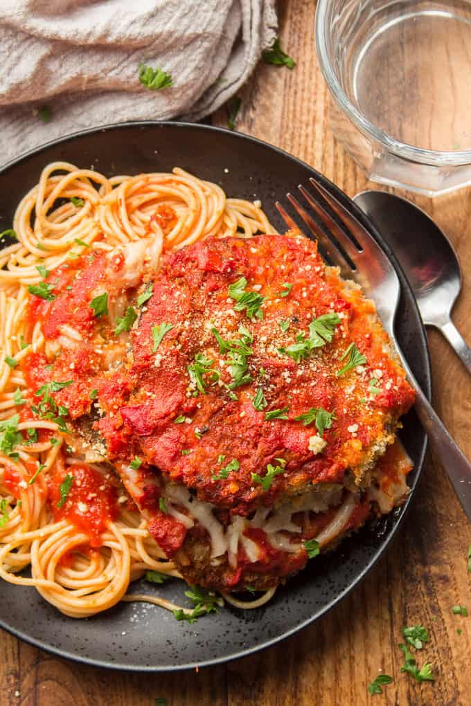 Close Up of Vegan Eggplant Parmesan Over Pasta on a Black Plate