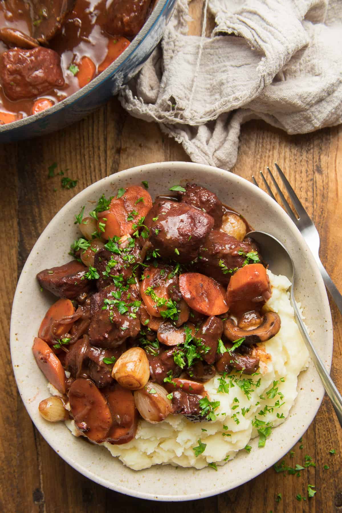 Wooden surface set with bowl of Vegan Coq au Vin and mashed potatoes with fork and knife.