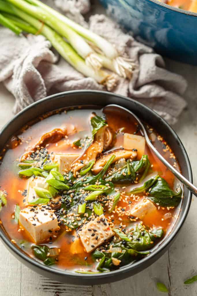 Bowl of Korean Tofu Soup with scallions and blue pot in the background.