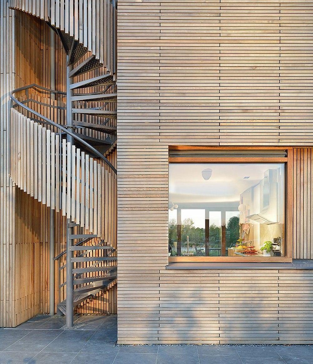 A modern wood house has an exterior spiral staircase that's covered in wood slats.