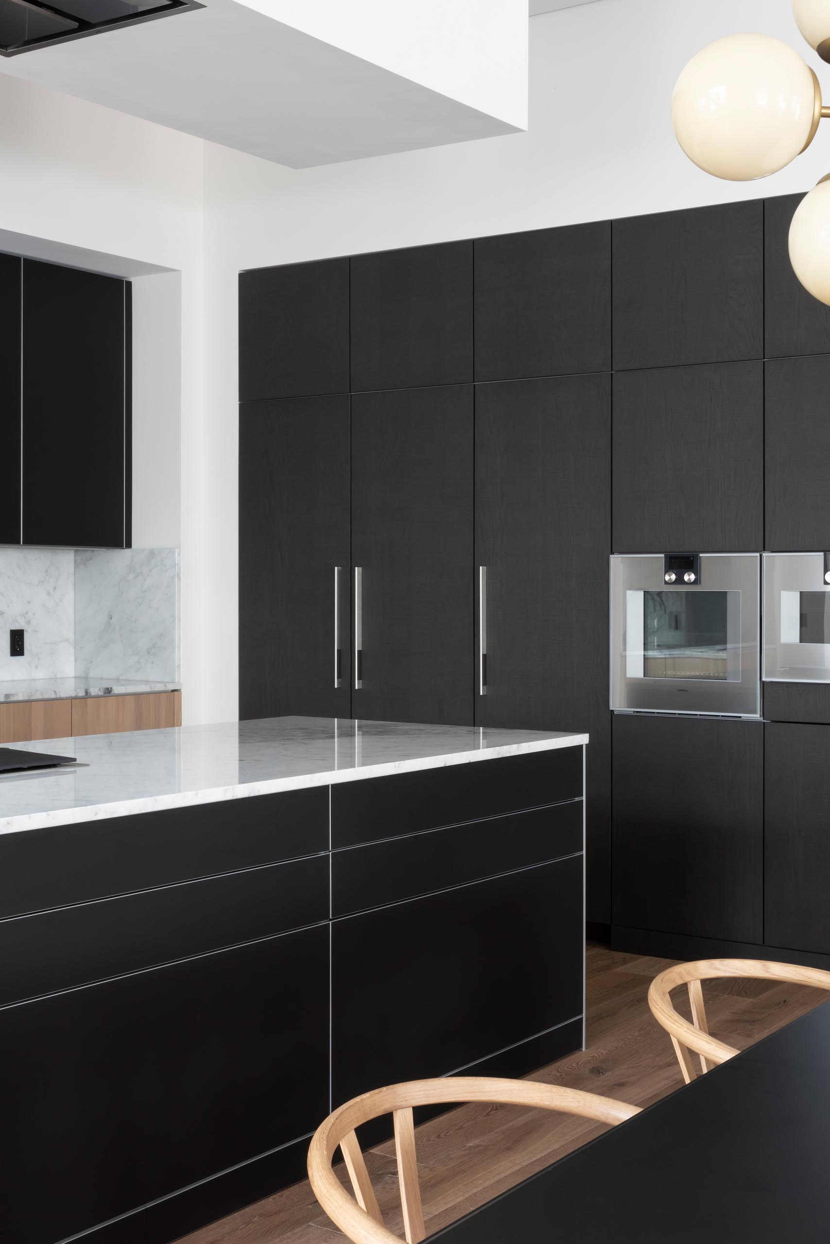 In this modern kitchen, matte black cabinets are complemented by gray marble countertops and backsplash.