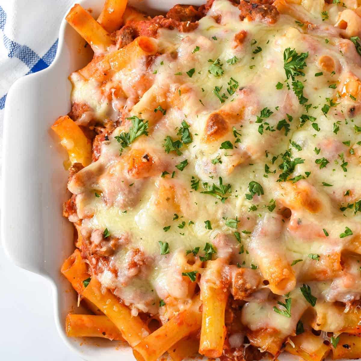 The finished baked ziti with sausage garnished with chopped parsley in a white casserole dish.