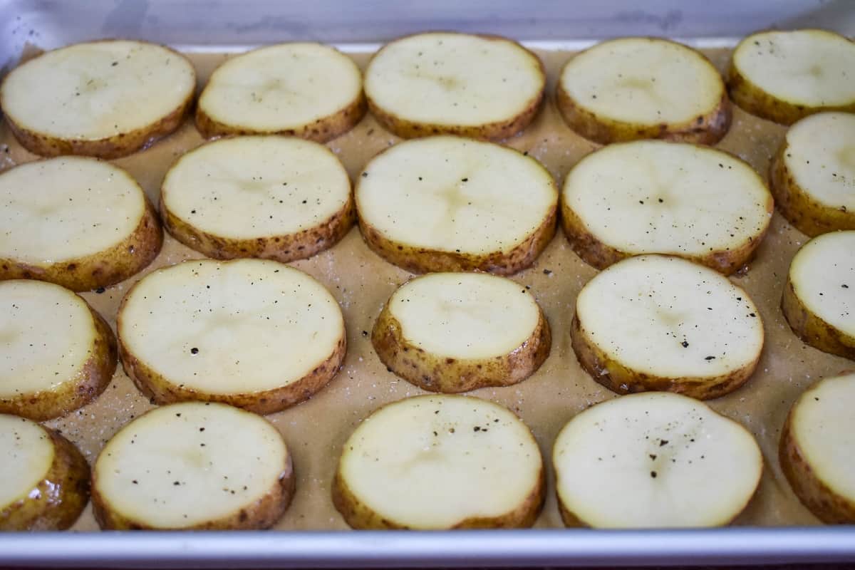 Potato slices arranged in rows on a parchment lined baking sheet.