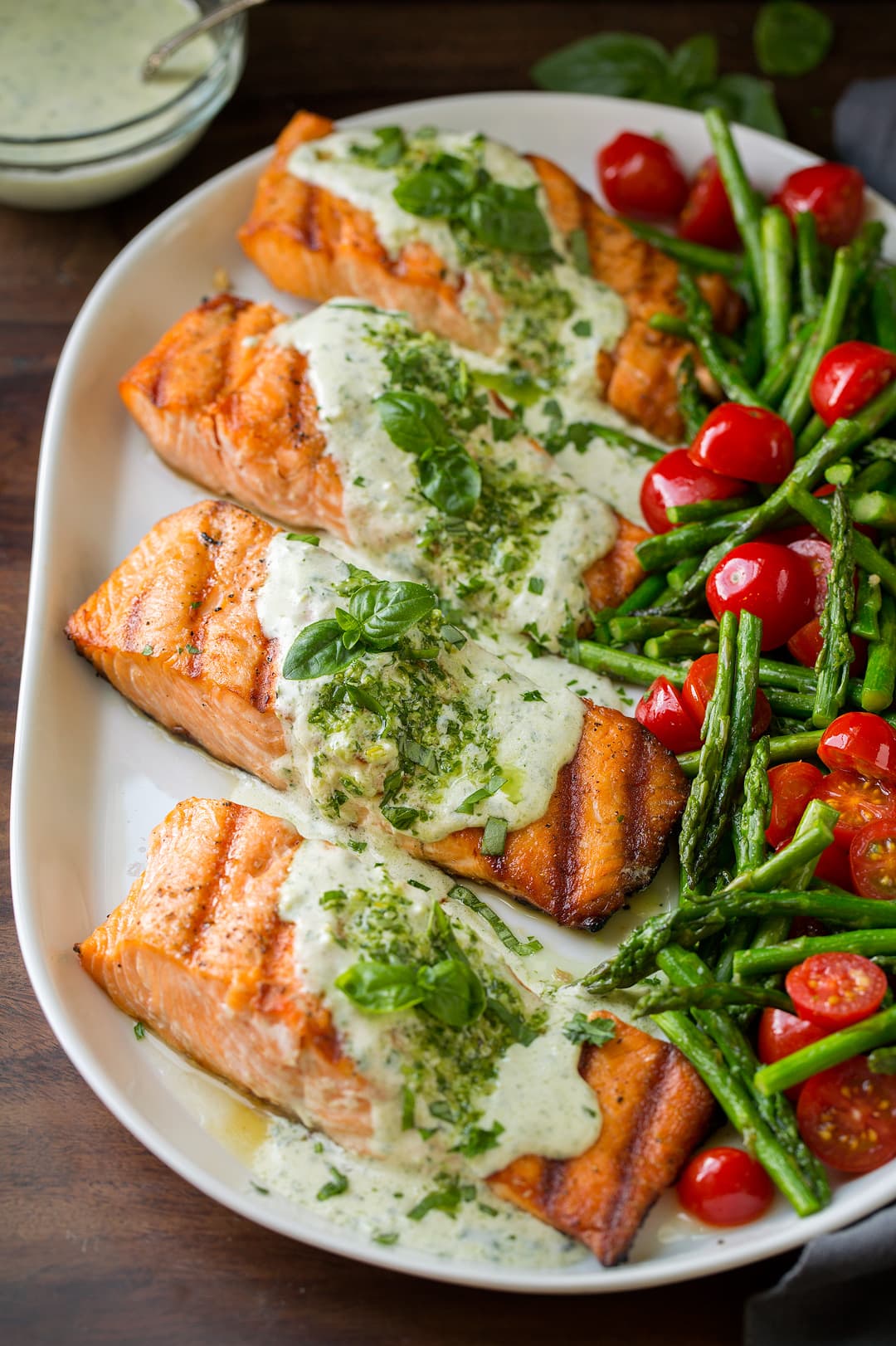 four Grilled Salmon fillets with Creamy Pesto sauce on serving plate with tomatoes and asparagus