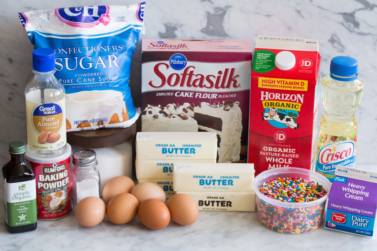 Funfetti Birthday Cake ingredients including cake flour, butter, sugar, eggs, egg whites, vanilla, almond extract, milk, sprinkles, vegetable oil, cream, salt, baking powder and powdered sugar.