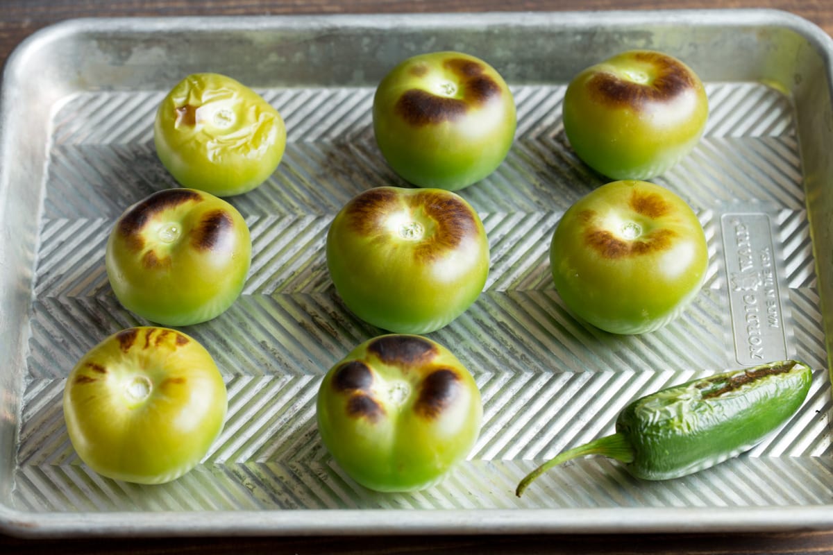 Roasted tomatillos and jalapeno on a baking sheet.