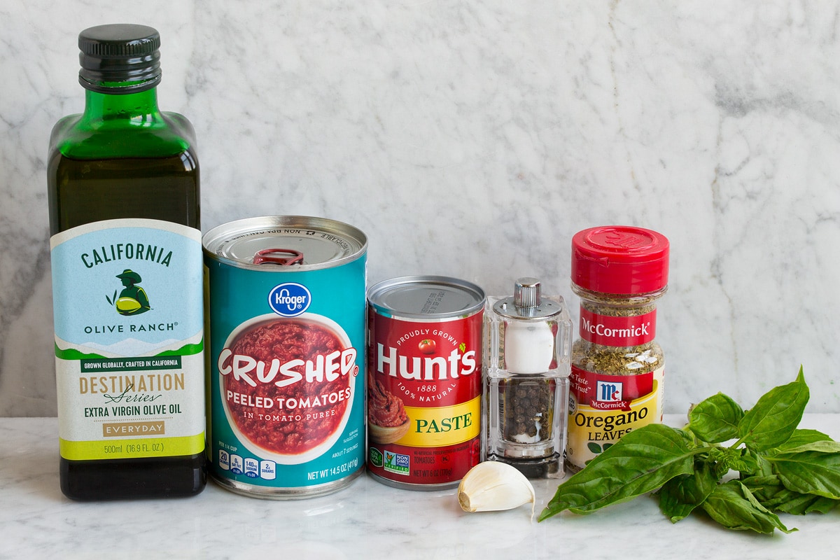 Ingredients used to make shown including olive oil, crushed tomatoes, tomato paste, salt and pepper, dried oregano, fresh basil, garlic, salt and pepper.