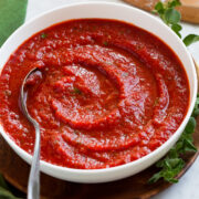 Homemade pizza sauce in a bowl with pizza dough in the background.