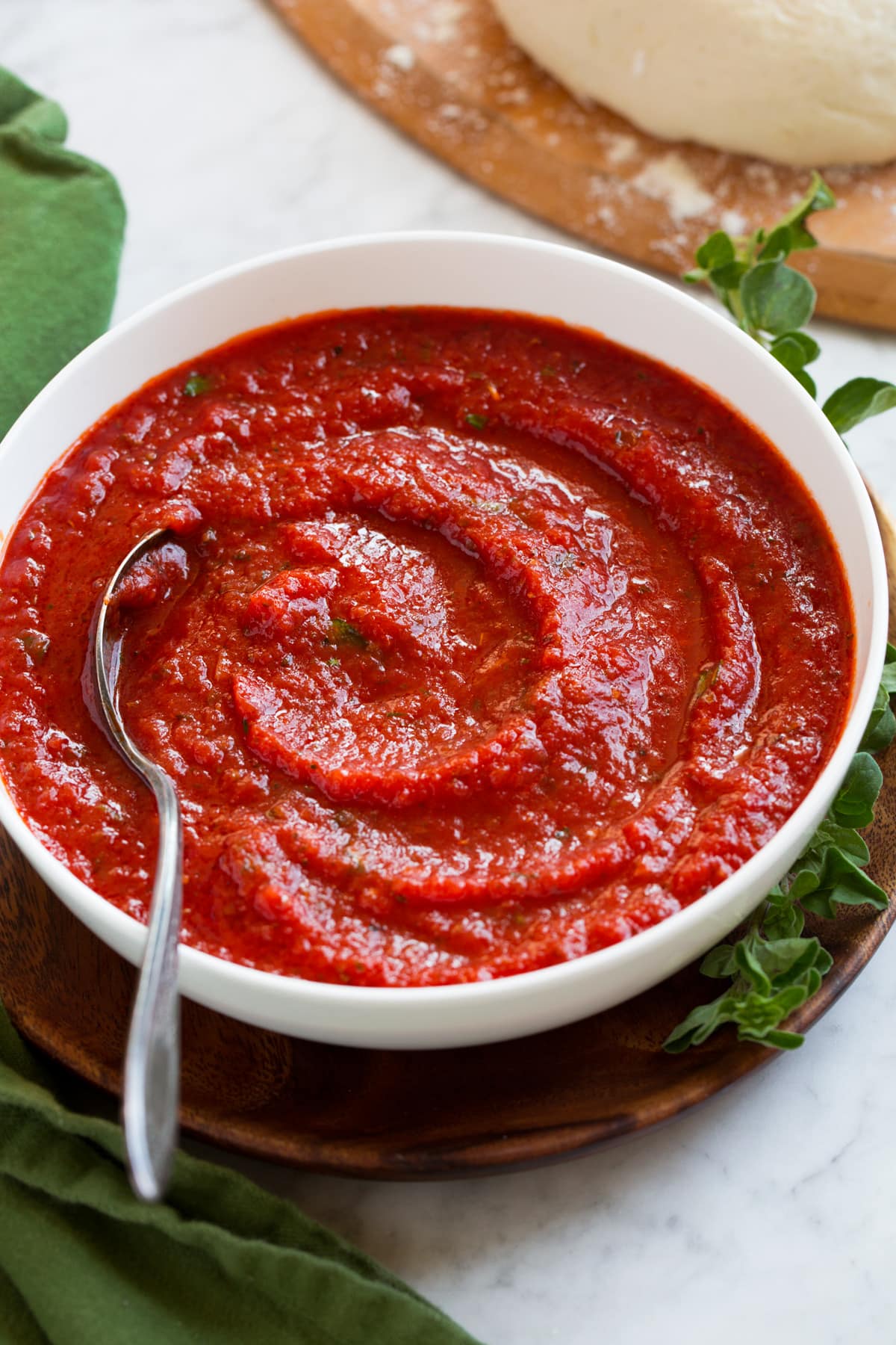 Homemade pizza sauce in a bowl with pizza dough in the background.