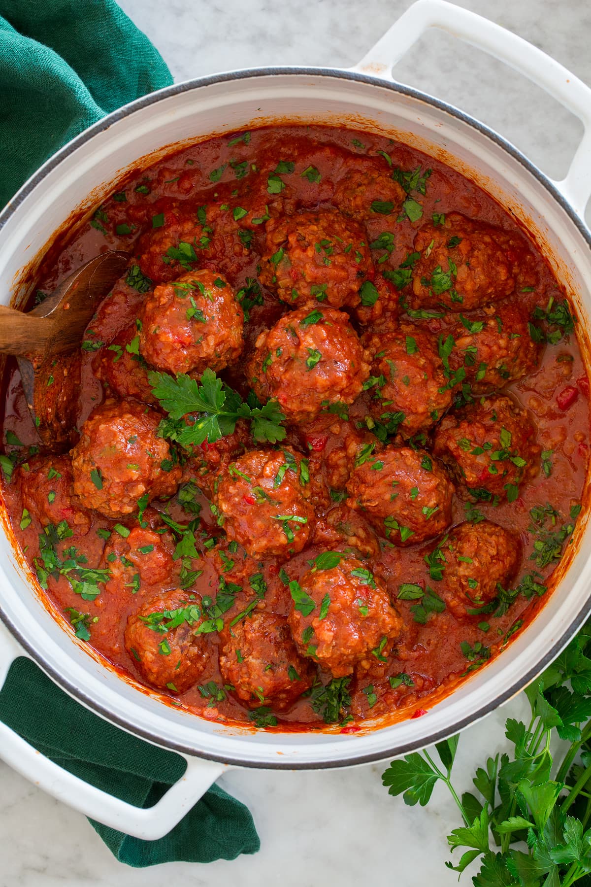 Overhead photo of Porcupine Meatballs in tomato sauce in a large white pot set over a marble surface with a green cloth to the side.