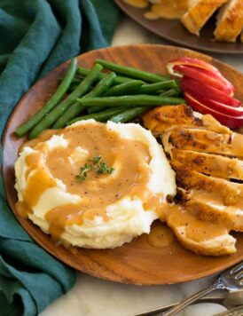 Chicken gravy shown on mashed potatoes with a side of roasted chicken, apples and green beans as a serving suggestion.