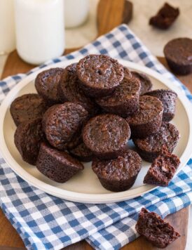 Homemade brownie bites stacked together on a plate over a blue checkered napkin.