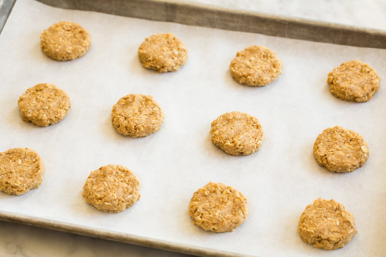 Oatmeal cookies shown before baking on parchment lined baking sheet.