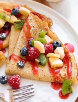 Close up photo of healthy oat crepes with chopped fruit and berry syrup.