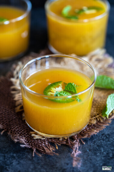 yellow color drink served in a glass garnished with mint and jalapeño