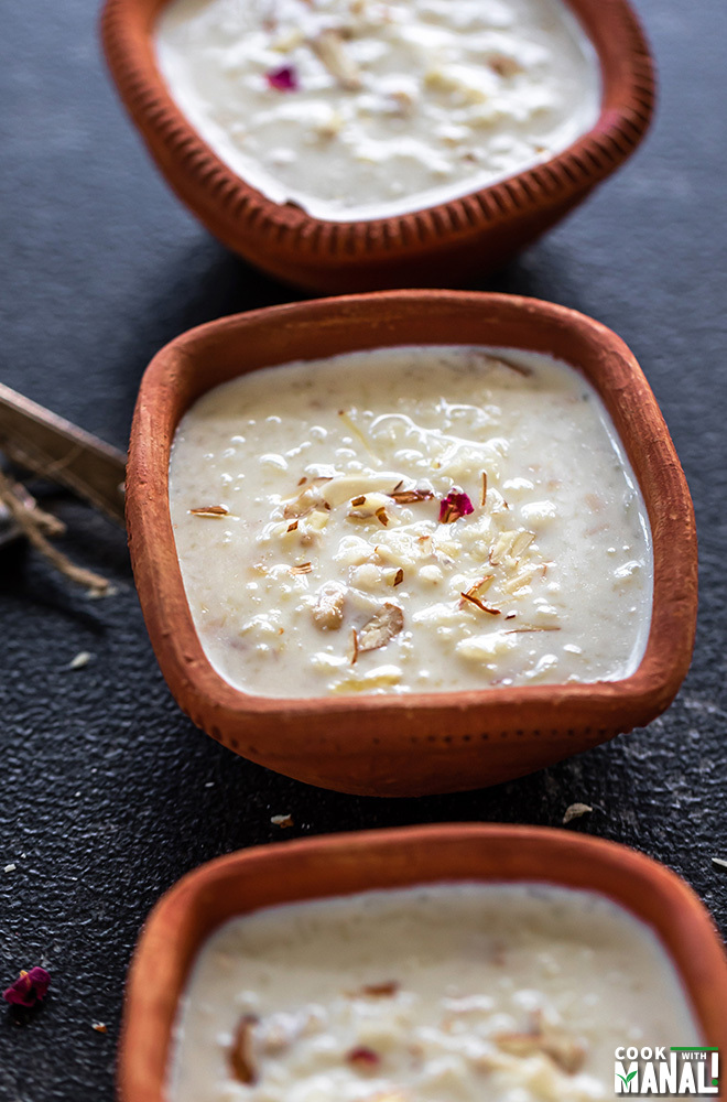 Kheer served in a clay bowl with 2 spoons on the side and more bowls of kheer on the side