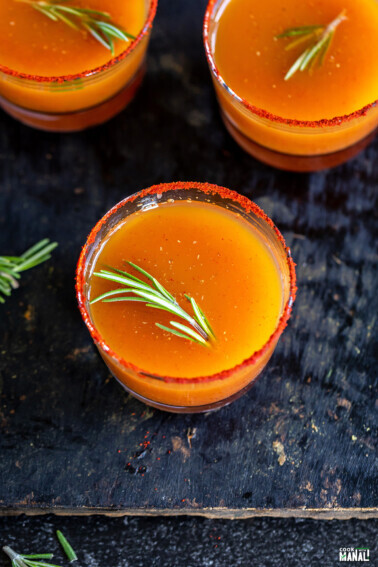 orange color drink garnished with rosemary served in short glasses