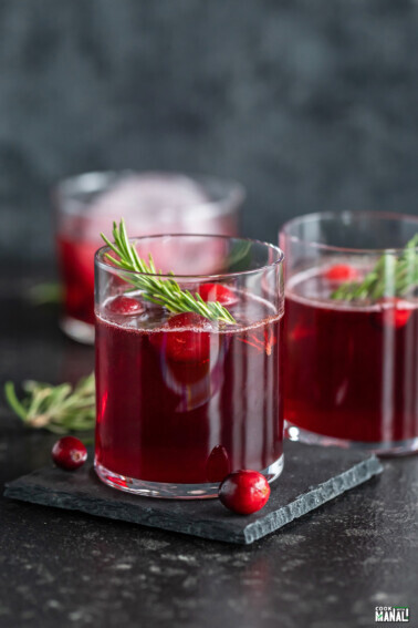 red color drink in a glass topped with fresh cranberries and rosemary