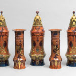 A collection of five burnt orange vases, each with unique ornamental designs in red, blue, and yellow.