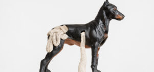 A sculpture of a dark brown dog looks to the right, hanging out of its middle and the back are what appears to be its insides (in cream) spilling out.