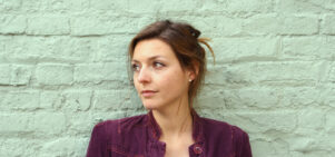 Portrait of Rebecca Watts who is white with brown hair in a purple shirt against a green wall