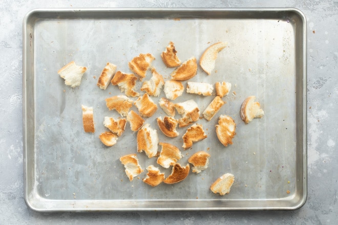 Torn bread pieces on a silver baking sheet.