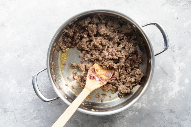 Ground sausage and vegetables cooking in a silver pot.