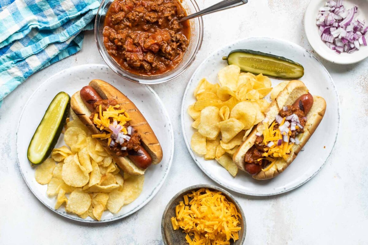 A chili dog on a plate with a pickle and chips.