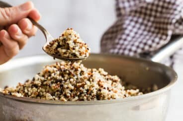 Cooked quinoa in a sliver bowl with someone spooning some out.